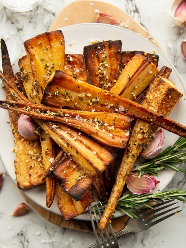 overhead shot of roasted parsnips served on small white plate garnished with fresh rosemary and garlic