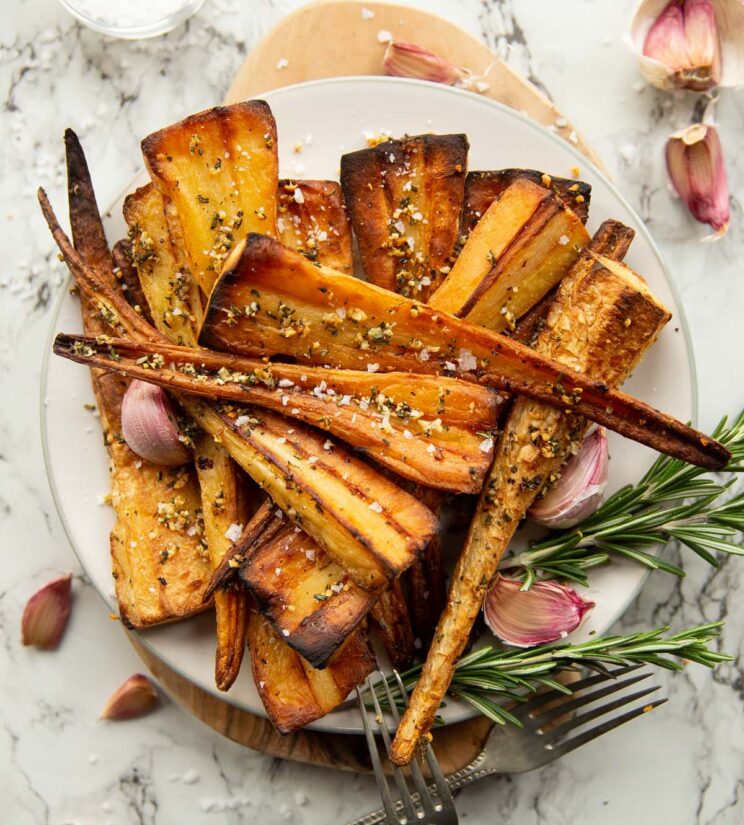 overhead shot of roasted parsnips served on small white plate garnished with fresh rosemary and garlic