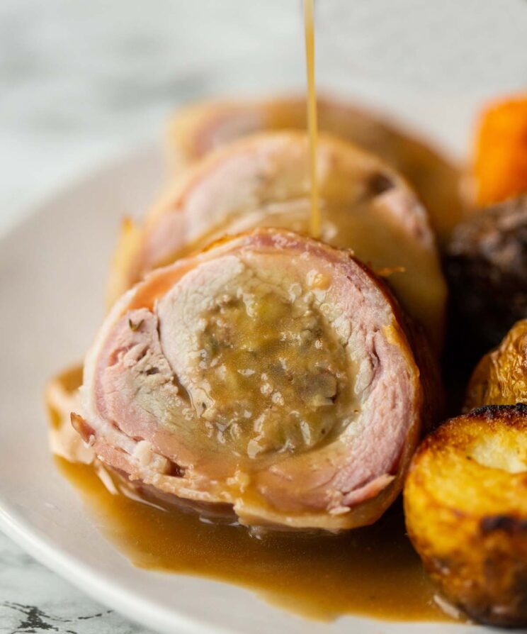 close up shot of stuffed pork tenderloin on small white plate with gravy drizzled over