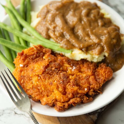 fried chicken cutlet served on small white plate with green beans, mash and gravy