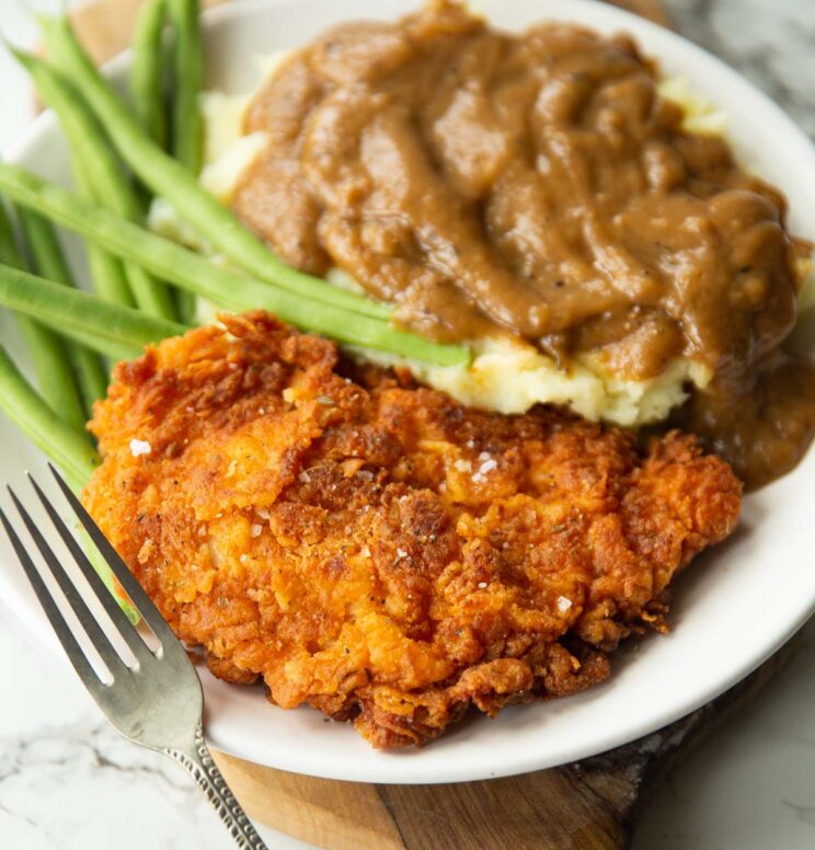 fried chicken cutlet served on small white plate with green beans, mash and gravy