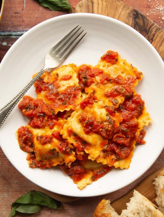 overhead shot of ravioli served on small white plate on wooden board with silver fork