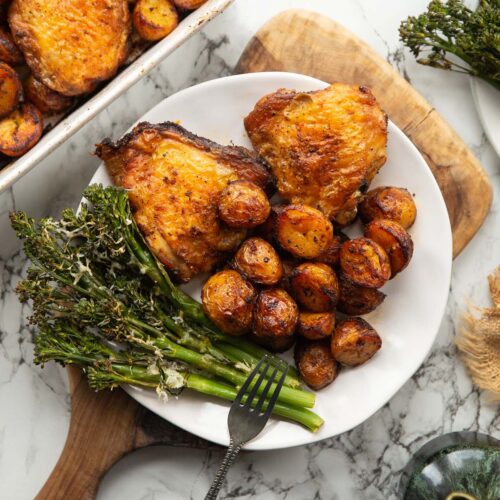 overhead shot of baked chicken and potatoes served on small white plate with tenderstem broccoli