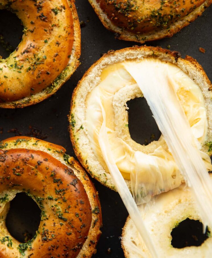 overhead close up shot of 4 cooked bagels on baking tray with one showing cheese filling