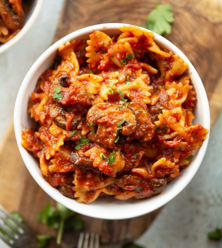 overhead shot of mushroom tomato pasta in small white bowl on wooden chopping board