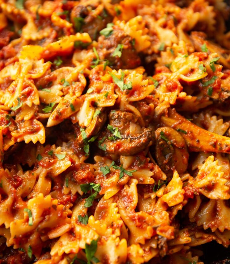 close up shot of tomato and mushroom pasta in skillet with wooden spoon digging in