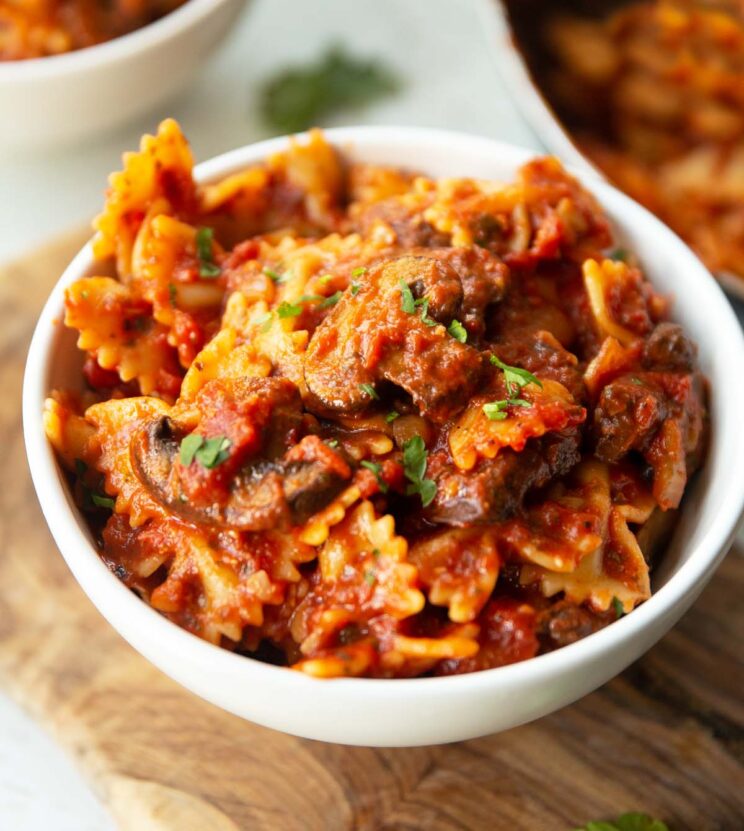 close up side shot of how to make tomato mushroom pasta in small white bowl garnished with fresh parsley