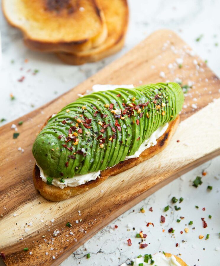 close up shot of avocado cream cheese toast on chopping board surrounded by garnish