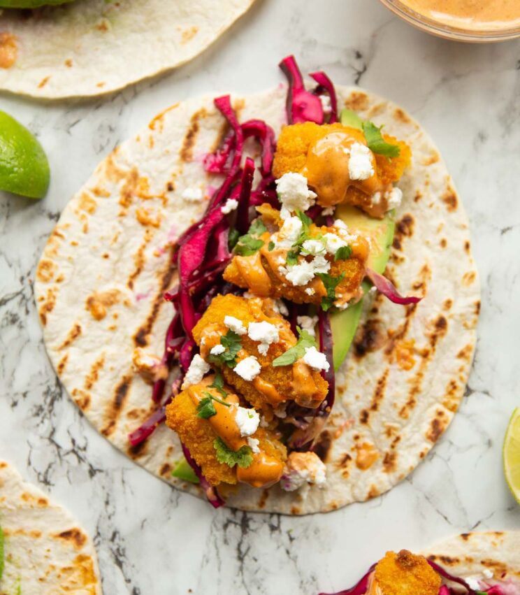 overhead close up shot of fish finger taco on marble background surrounded by garnish