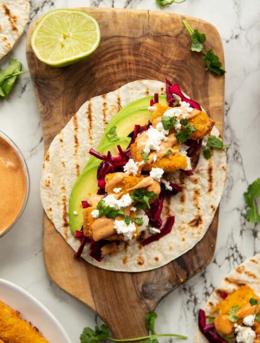 overhead shot of fish finger taco on wooden board surrounded by garnish