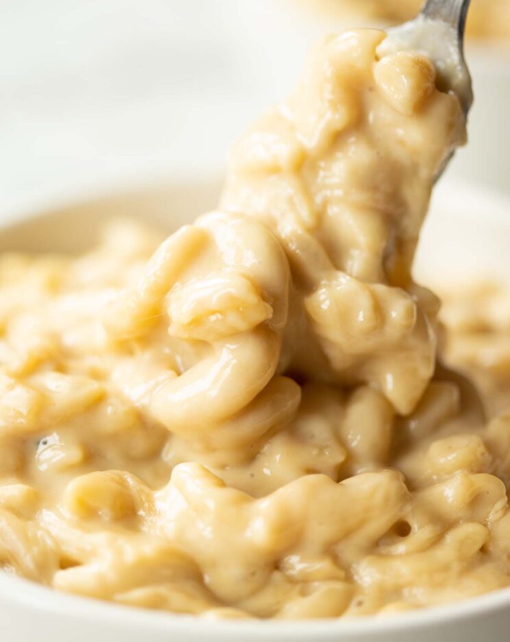 close up shot of fork digging into small white bowl of mac and cheese