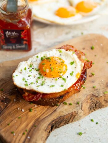 fried egg on toast on wooden board with chilli jam and fried eggs blurred in background