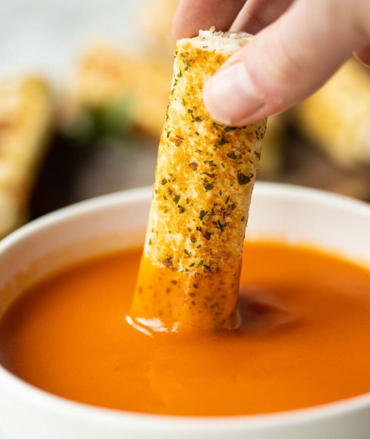 hand dunking in garlic bread roll ups into small white bowl of tomato soup