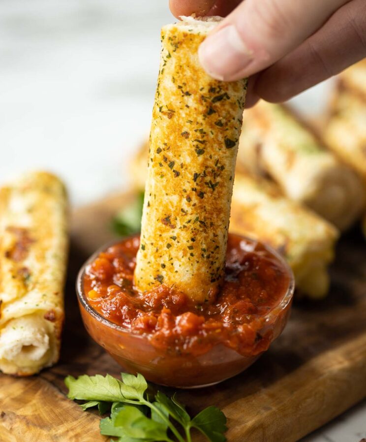 hand dunking garlic bread roll up into small glass jar of marinara sauce