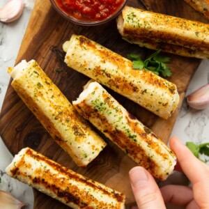 overhead shot of garlic bread roll ups on wooden chopping board with hand taking one