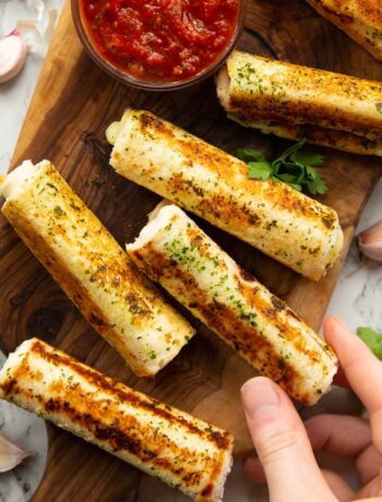overhead shot of garlic bread roll ups on wooden chopping board with hand taking one