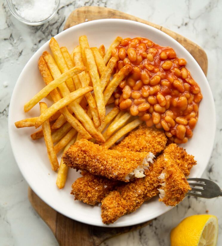 overhead shot of fish fingers, chips and beans on small white plate