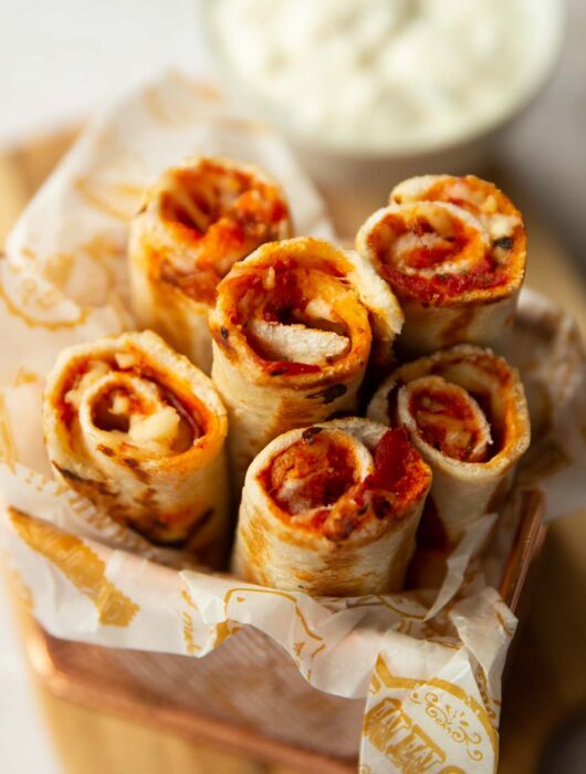 6 pizza roll ups in a small pot with dip blurred in the background