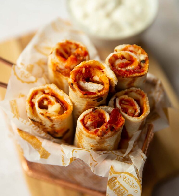 6 pizza roll ups in a small pot with dip blurred in the background