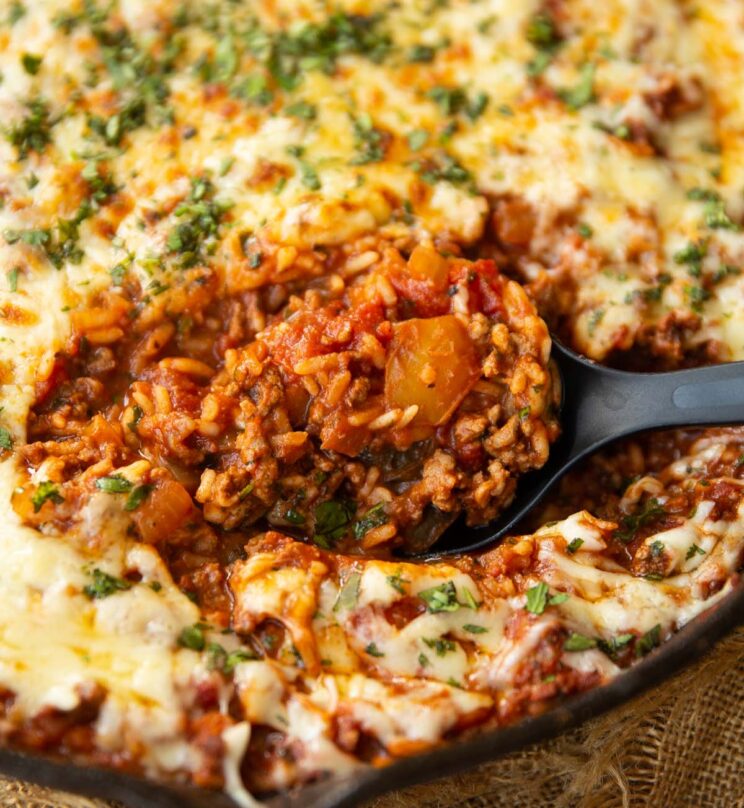 close up shot of black serving spoon digging into skillet of stuffed pepper casserole