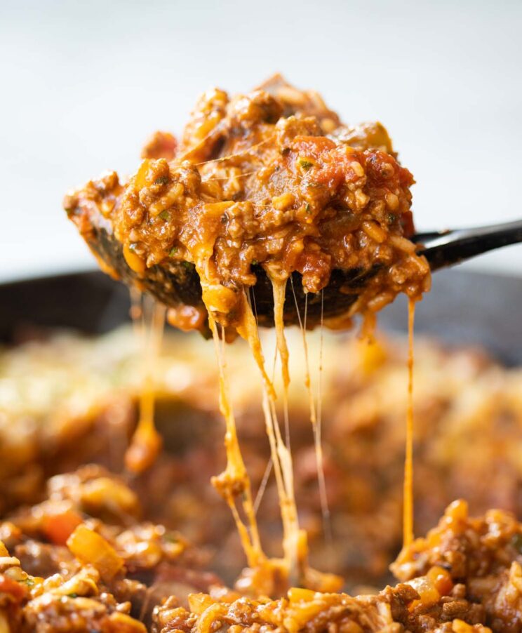 side shot of black serving spoon scooping unstuffed peppers out of cast iron skillet with cheese dripping down