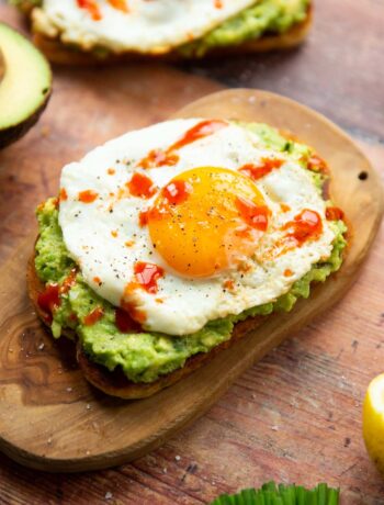 close up shot of avocado egg toast on small chopping board surrounded by garnish