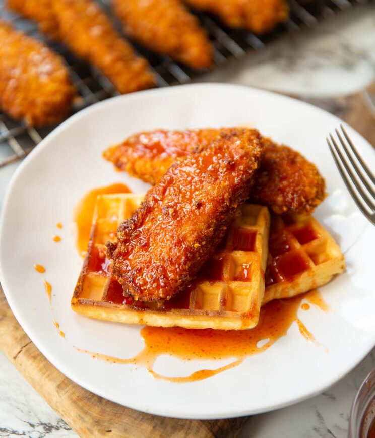 2 cornflake fried chicken tenders on two waffles with sriracha maple syrup on small white plate