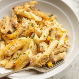 close up shot of creamy tuna pasta bake in white bowl with silver fork digging in