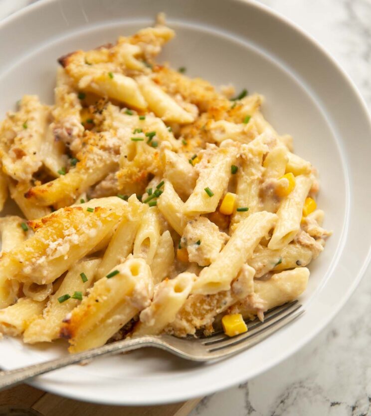 close up shot of creamy tuna pasta bake in white bowl with silver fork digging in