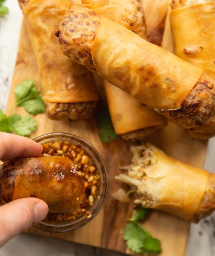 overhead shot of spring rolls on chopping board with hand dunking half into dip