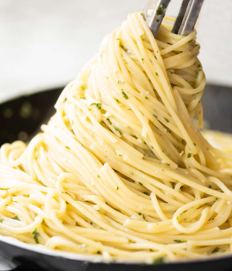 close up shot of pasta tongs tossing garlic butter pasta in skillet