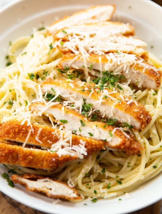 close up shot of garlic chicken pasta served with parmesan and parsley in white dish