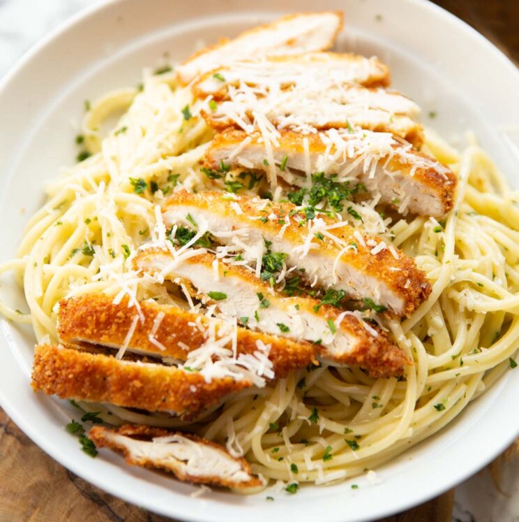 close up shot of garlic chicken pasta served with parmesan and parsley in white dish