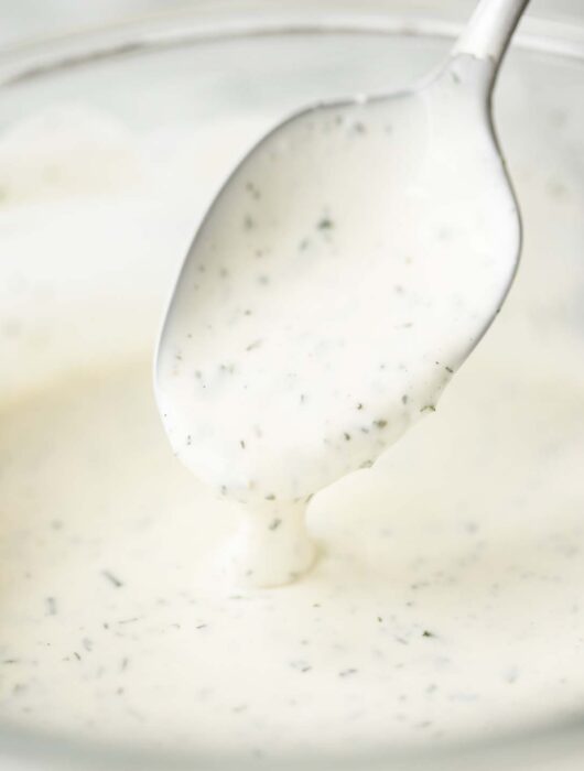 close up shot of silver spoon digging into glass bowl of ranch