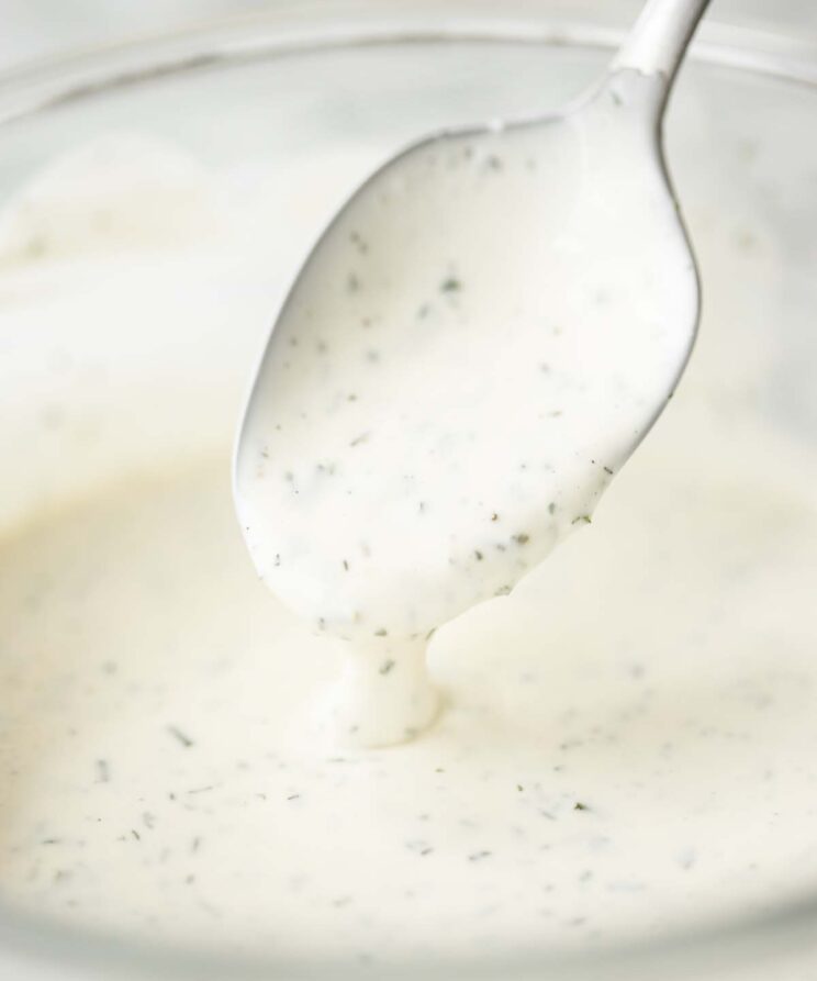close up shot of silver spoon digging into glass bowl of ranch