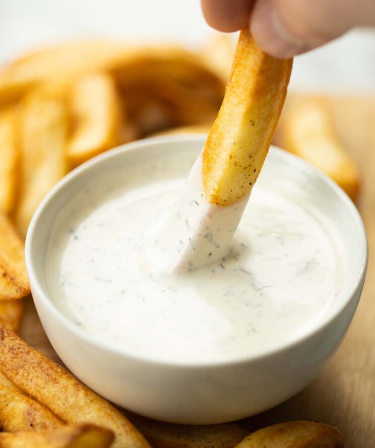 hand dunking chip into small white pot of homemade ranch dip
