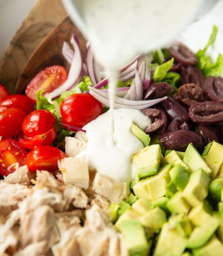 close up shot of small jug pouring homemade ranch dressing into big bowl of salad