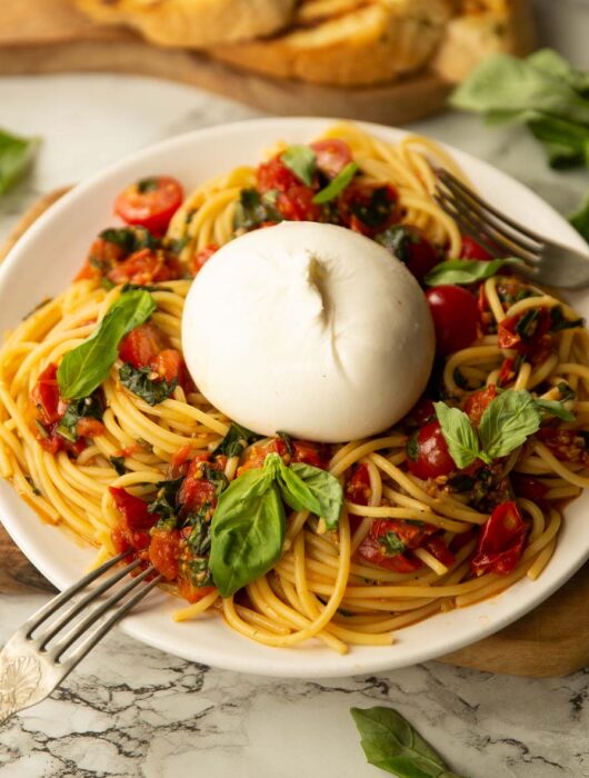 side shot of burrata caprese pasta on small white plate garnished with fresh basil