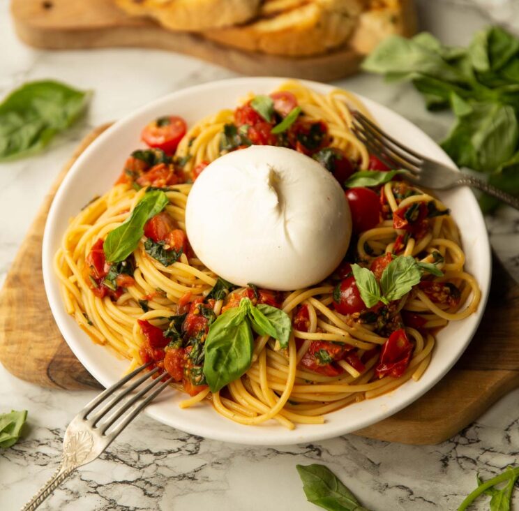 side shot of burrata caprese pasta on small white plate garnished with fresh basil