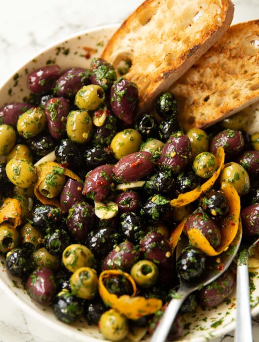 close up shot of large white dish with marinated olives and two slices of toasted ciabatta