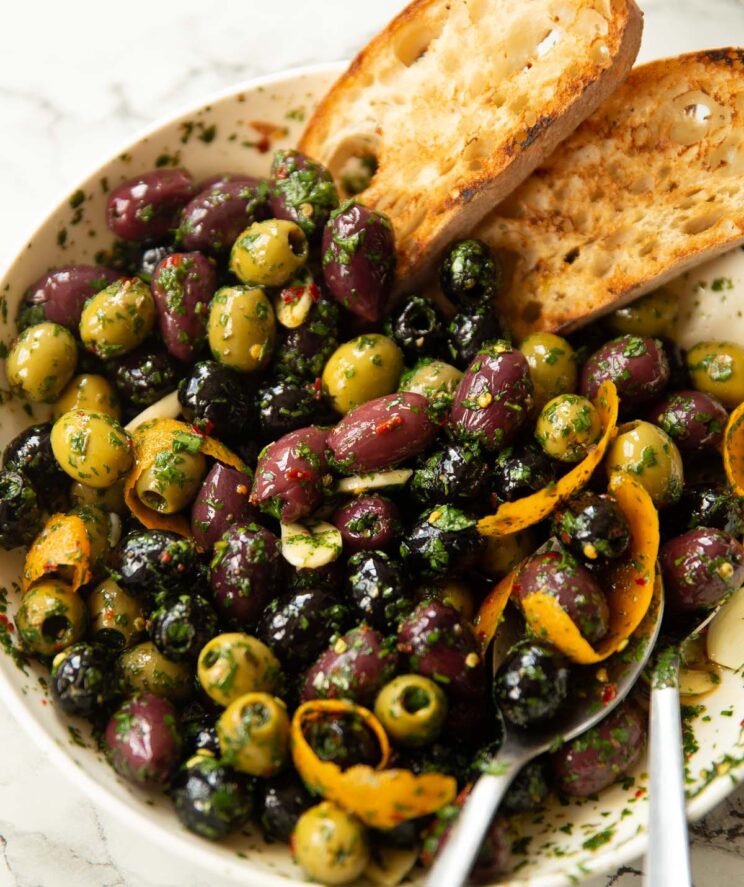 close up shot of large white dish with marinated olives and two slices of toasted ciabatta