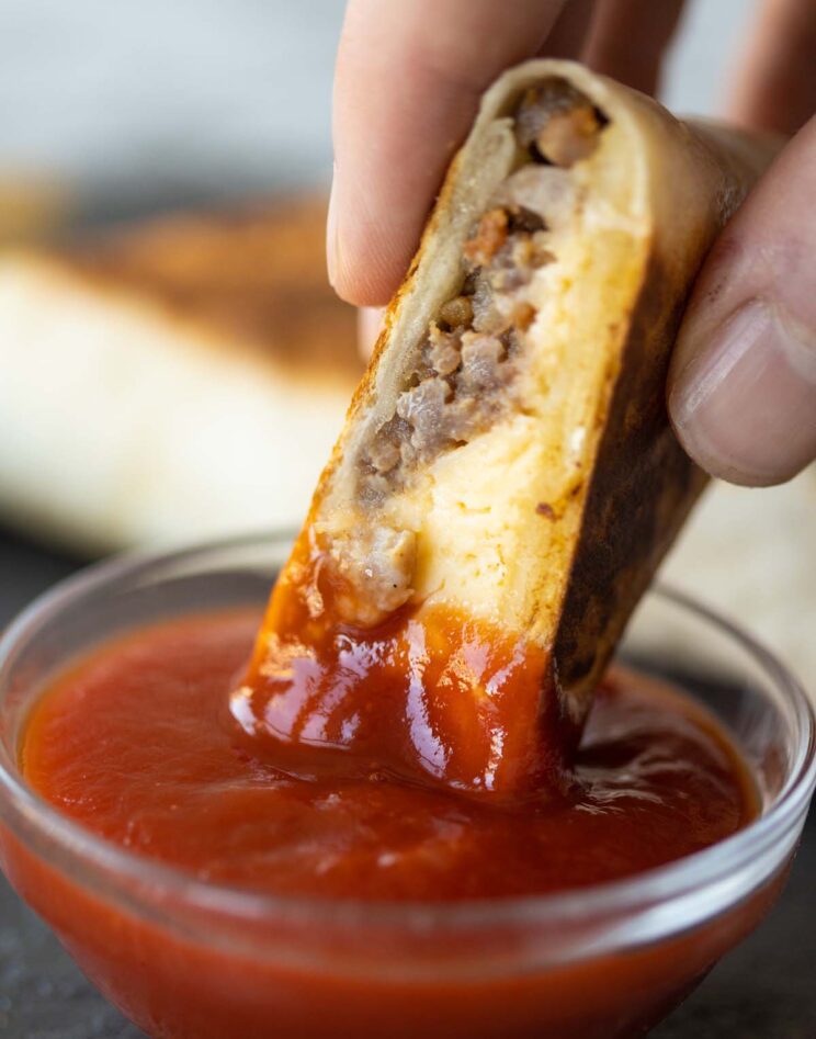 close up shot of hand dunking breakfast tortilla pocket into small glass pot of ketchup