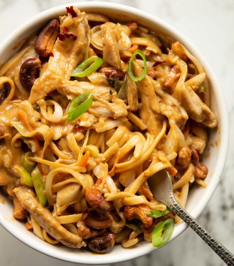close up overhead shot of cashew butter chicken noodles in small with bowl with silver fork digging in