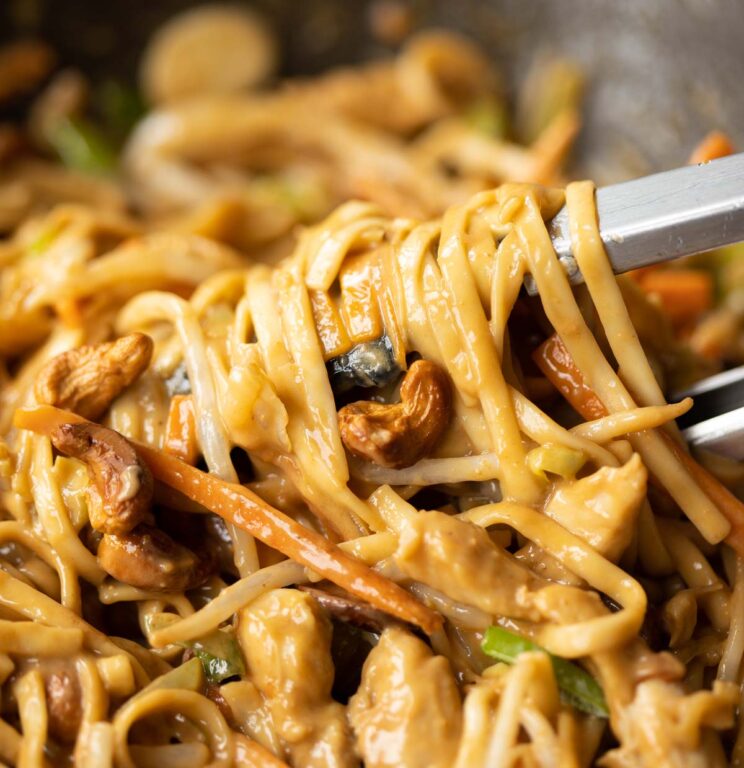 close up shot of tongs twisting cashew chicken noodles in small wok