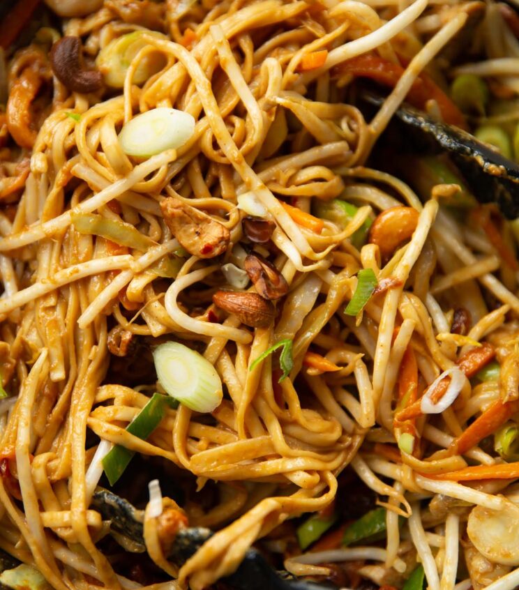 close up shot of cashew chicken stir fry in wok with tongs digging in