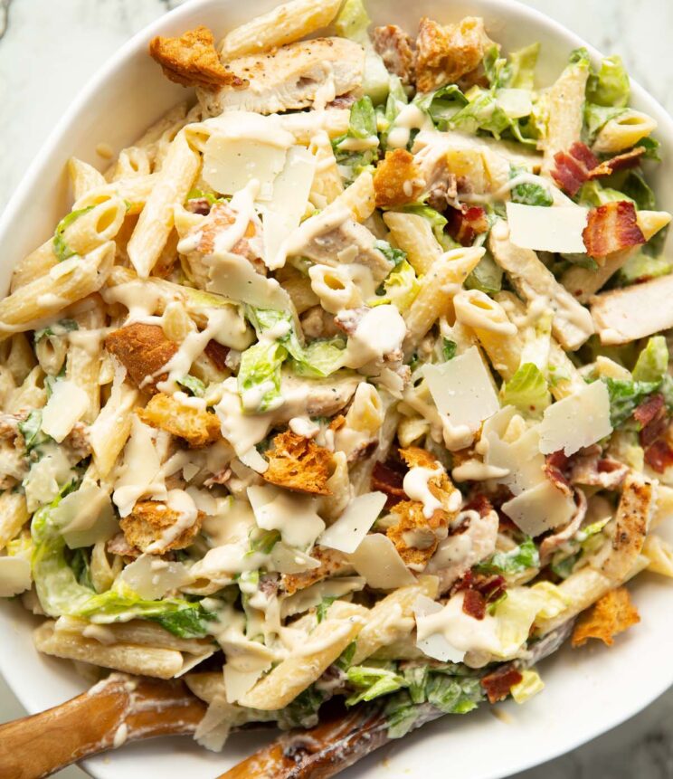 close up overhead shot of chicken caesar pasta salad in large white bowl with wooden salad tossers