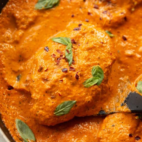 close up shot of creamy roasted red pepper chicken in large pan with spatula lifting chicken