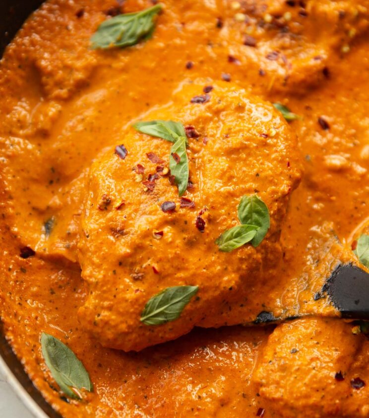 close up shot of creamy roasted red pepper chicken in large pan with spatula lifting chicken