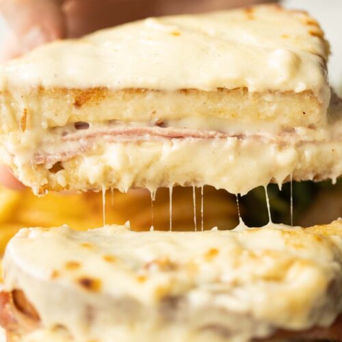 close up shot of hand lifting half of croque monsieur showing filling