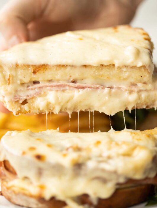 close up shot of hand lifting half of croque monsieur showing filling